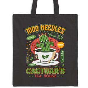 Puede incluir: Bolso tote negro con un diseño caprichoso para "Cactuar's Tea House". El diseño incluye un cactus verde en una taza de té, con texto que dice "1000 Needles Green Tea" y "Cactuar's Tea House". El bolso tiene dos asas negras.