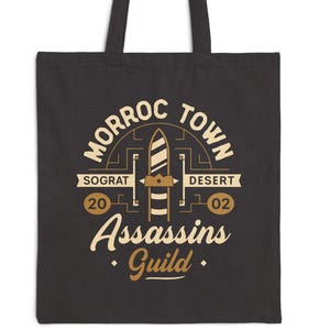 May include: Black tote bag with a graphic design featuring the text "MORROC TOWN" and "ASSASSINS GUILD" in a vintage style. The design includes a central emblem with a stylized arrow and the words "Sograt" and "Desert".