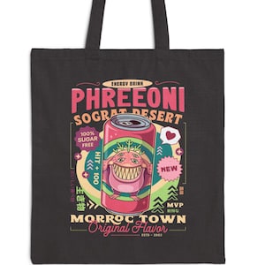 May include: Black tote bag featuring a colorful graphic of a soda can with the text "PHREEONI SOGRAT DESERT". The can has a cartoon monster design and the words "MORROC TOWN Original Flavor". The bag has black handles.