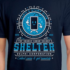 May include: Navy blue t-shirt with a circular graphic featuring a smiling phone character and the text "Cabin's Stamp Club." The design includes the words "Shelter" and "Delphi Corporation" in white and blue. The shirt also has the text "Collect coins & get rewards."