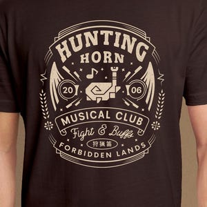 Peut inclure: Un t-shirt à manches courtes marron foncé avec une impression graphique beige. Le motif comprend le texte "HUNTING HORN MUSICAL CLUB", "Fight & Buffs", "FORBIDDEN LANDS", les chiffres "20" et "06", une note de musique et des caractères japonais.