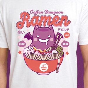 May include: White t-shirt with a cartoon bat eating ramen. The text "Geffen Dungeon Ramen" is above the bat. The text "ESTD 2002" is below the bat. The text "デビルチ NEW" is to the right of the bat.
