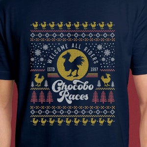 Puede incluir: Una camiseta azul marino con un diseño festivo que presenta un Chocobo amarillo y blanco, un tipo de ave de la serie de videojuegos Final Fantasy. El diseño incluye el texto "Welcome All Riders", "ESTD 1997" y "Chocobo Races".