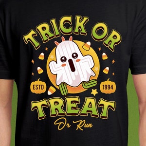 Puede incluir: Camiseta negra con un diseño de Halloween. El diseño presenta un fantasma de dibujos animados con las palabras "Trick or Treat" en verde y amarillo. La camiseta también incluye el texto "ESTD 1994" y caramelos.