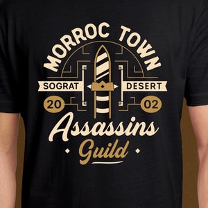 May include: Black t-shirt with a gold graphic design featuring the text "Morroc Town Assassins Guild" with a stylized sword and the words "Sograt 20" and "Desert 02".