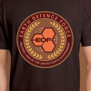 May include: A black t-shirt with a brown and gold circular logo that says "Earth Defence Force" and "Military Arm of the United Earth Government". The logo features a stylized honeycomb design with the letters "EDF" in the center.