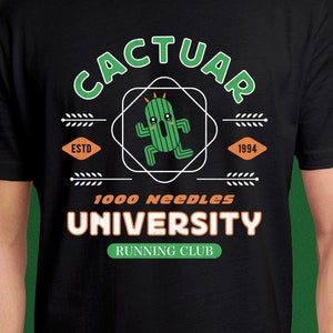 Puede incluir: Camiseta negra con un personaje de cactus verde que lleva una diadema blanca y corre. El texto "Cactuar 1000 Needles University Running Club" está impreso en la camiseta. El texto "Estd 1994" también está impreso en la camiseta.