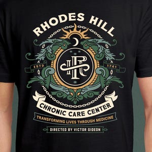 May include: Black t-shirt featuring a detailed emblem with the text "RHODES HILL" above a circular design. The design includes the text "CHRONIC CARE CENTER" and "TRANSFORMING LIVES THROUGH MEDICINE". The shirt also has the text "DIRECTED BY VICTOR GIDEON".