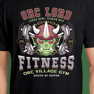 May include: Black t-shirt with a graphic featuring an Orc character wearing a horned helmet and lifting weights. The design includes the text "ORC LORD FITNESS" and "ORC VILLAGE GYM SOUTH OF GEFFEN". The design is in shades of green, red, white, and gray.