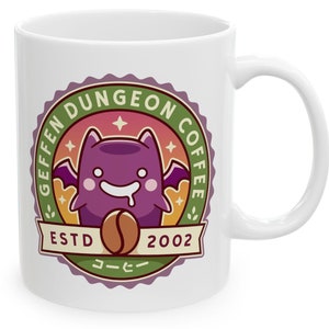 May include: White ceramic coffee mug with a green, purple, and orange circular design. The design features a cartoon bat holding a coffee bean and the text "Geffen Dungeon Coffee EstD 2002".