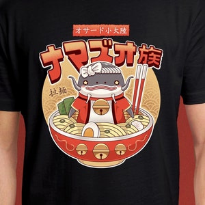 Puede incluir: Camiseta negra con un pez gato de dibujos animados que lleva un kimono rojo y dorado en un cuenco de fideos ramen. El texto "オサード小太郎" y "ナマズカ様" está impreso en la camiseta.