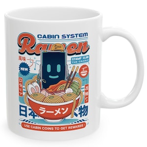 May include: White ceramic mug featuring a colorful illustration of a bowl of ramen with chopsticks, a smiling robot, and Japanese text. The mug has a curved handle and the words "Cabin System Ramen" are displayed.