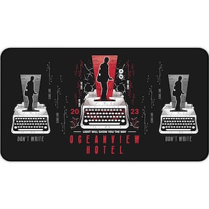 May include: Black rectangular desk mat with a graphic design featuring typewriters and a person's silhouette. The text "DON'T WRITE" is on the left and right, and "OCEANVIEW HOTEL" is at the bottom, with the numbers 20 and 23.