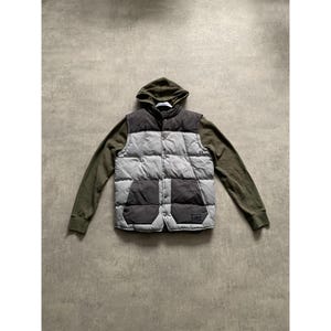 Puede incluir: Un chaleco con capucha en gris, negro y verde oliva. El chaleco tiene un diseño acolchado y dos bolsillos delanteros. Las mangas y la capucha son de color verde oliva. Prenda de abrigo.