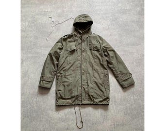 May include: An olive green hooded jacket with a drawstring waist and multiple pockets. The jacket has a button-up front and long sleeves with buttoned cuffs. A hanger is visible near the jacket.
