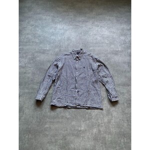 May include: A long-sleeve button-down shirt featuring a repeating dark blue and white geometric pattern. The shirt has a standard collar, a front button placket, and a small dark embroidered logo on the left chest area above the pocket.