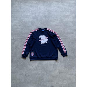 May include: Navy blue sweatshirt with red and white stripes on the sleeves. The sweatshirt features a white graphic with text and a team logo on the chest. A classic athletic style.