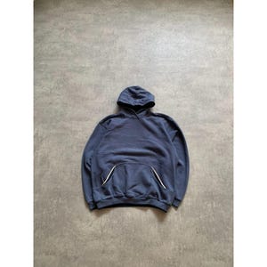 May include: A navy blue hoodie with a hood and a kangaroo pocket. The pocket has white trim. The hoodie is made of a soft material and is laid flat on a gray surface.