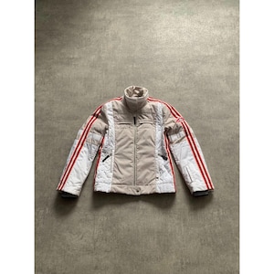 May include: A beige and white winter jacket with red stripes down the sleeves. The jacket has a high collar, a zipper closure, and black accents. The jacket is designed for cold weather and outdoor activities.