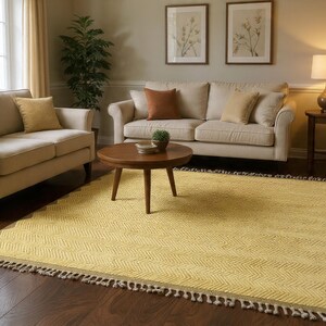 Può includere: Soggiorno con tappeto giallo fantasia, tavolino rotondo in legno e due divani beige con cuscini. La stanza ha pavimenti in parquet ed è ben illuminata. Il tappeto ha un bordo a zig-zag.
