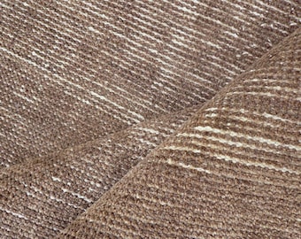 May include: Close-up of a brown and white woven textile. The fabric has a textured appearance with diagonal white stripes against a brown background. The textile is folded, revealing layers of the material.