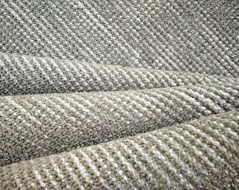 May include: Close-up of a rolled-up, textured fabric in shades of gray and white. The fabric has a diagonal pattern with a woven appearance. The texture is visible, with a mix of light and dark fibers creating a subtle contrast. The fabric appears to be soft and pliable.