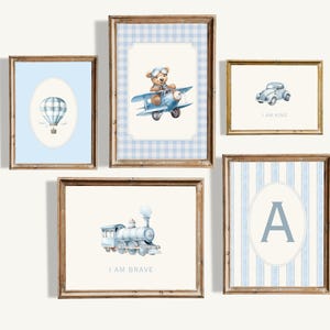 Peut inclure: Ensemble de six impressions encadrées avec des motifs vichy et rayés bleus et blancs. Chaque impression présente une illustration aquarelle différente d'un jouet pour enfant, notamment un ballon à air chaud, un ours en peluche dans un avion, une voiture, un train et la lettre A. Les impressions comprennent le texte "Je suis courageux", "Je suis gentil" et "A".