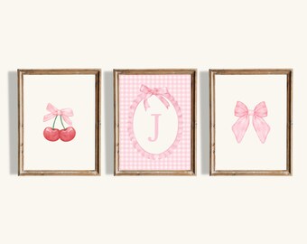 May include: Three framed watercolor prints with a light background. The prints feature a pair of cherries with a pink bow, a pink gingham oval with the letter "J" and a pink bow, and a pink bow.