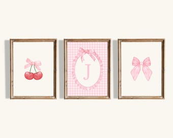 May include: Three framed prints with pink gingham backgrounds. The left print features two red cherries with a pink bow. The center print has a pink bow with a white circle and the letter "J" in pink. The right print has a large pink bow.