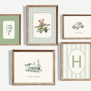 Peut inclure: Cinq impressions d'art encadrées avec une esthétique vintage. Les impressions présentent une montgolfière, un ours en peluche dans un biplan, une voiture, un train et la lettre "H". La palette de couleurs comprend des nuances de vert, de marron et de crème, avec les phrases "I AM KIND" et "I AM BRAVE".