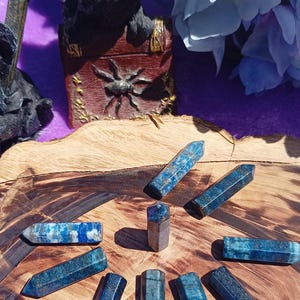 May include: A collection of ten blue and grey lapis lazuli crystal wands arranged in a circle on a wooden surface.