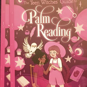May include: A pink book cover with the title "The Teen Witches' Guide to Palm Reading". The cover features two young women, one with brown skin and the other with white skin, both wearing pink dresses and holding hands. The background is a dark purple with stars and other magical symbols.