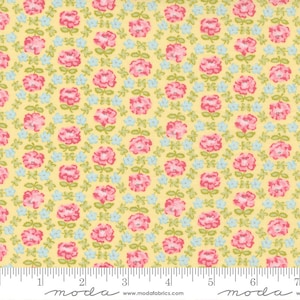 May include: Yellow fabric with a repeating pattern of pink roses and small blue flowers. Green leaves and stems connect the flowers. The fabric has a ruler along the bottom edge.