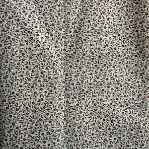 May include: A fabric featuring a dense, repeating pattern of small dark brown flowers and delicate winding vines set against a solid off-white background. The intricate botanical print covers the entire surface with a consistent, uniform layout.