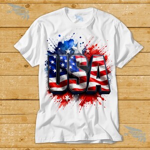 May include: White t-shirt featuring the word "USA" in a 3D design, with the letters colored in the American flag pattern. The shirt has a watercolor-style background with red, white, and blue splashes and stars.