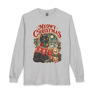 Puede incluir: Una camiseta gris jaspeado de manga larga con un gráfico de un gato negro que lleva un suéter rojo y blanco con copos de nieve, un lazo verde y un cascabel. El texto MEOWY CHRISTMAS aparece sobre el gato, rodeado de regalos y una taza.