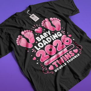 Puede incluir: Camiseta negra con un gráfico rosa que dice "Baby Loading 2026 Twins Double Trouble". El diseño incluye huellas de pies de bebé rosas, corazones y una barra de carga. Una etiqueta está adherida a la camiseta.