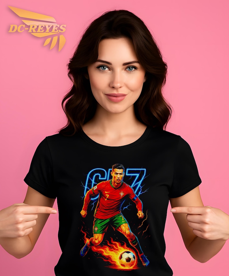 May include: Black t-shirt featuring a vibrant graphic of a soccer player in a red and green uniform, with the number 7 and the player's image. The design includes a soccer ball engulfed in flames and a neon blue outline. The shirt is worn by a person.