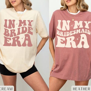 Può includere: Due magliette oversize con il testo "In My Bride Era" e "In My Bridesmaid Era" in un font retrò. Le magliette sono di colore crema morbido e malva bruciato.