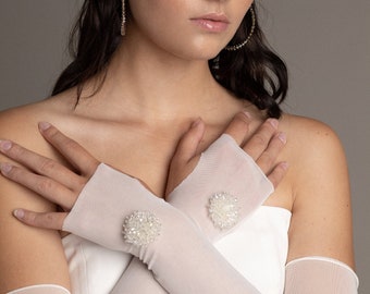 May include: White sheer long gloves with beaded embellishments. The gloves are worn by a person with dark hair and are crossed over the chest.