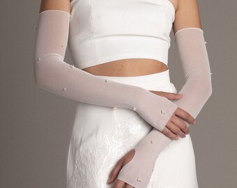 May include: A white strapless top with a white skirt. The top is cropped and the skirt has a floral design. The model is wearing white gloves with pearl embellishments.