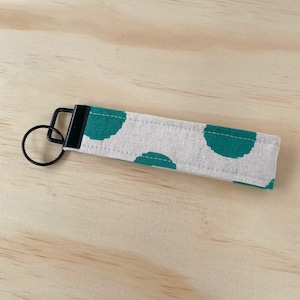 May include: A beige fabric key chain with a black metal ring and a green polka dot pattern.