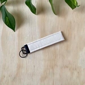 May include: A white fabric key chain with a pink polka dot pattern and a black metal key ring.