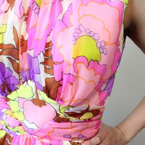 May include: A pink and brown sleeveless dress with a floral print. The dress has a high neck and a fitted bodice. The skirt is full and flowing.