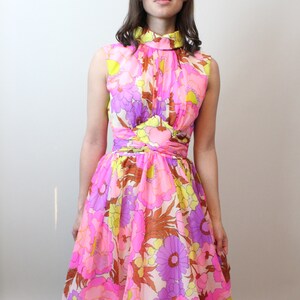 May include: A pink, yellow, and purple floral print dress with a high neck and a fitted bodice. The dress has a flared skirt and a scalloped hem.