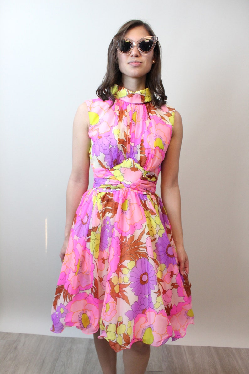 May include: A pink, yellow, and purple floral print dress with a high neck and a fitted bodice. The dress has a flared skirt and a scalloped hem.