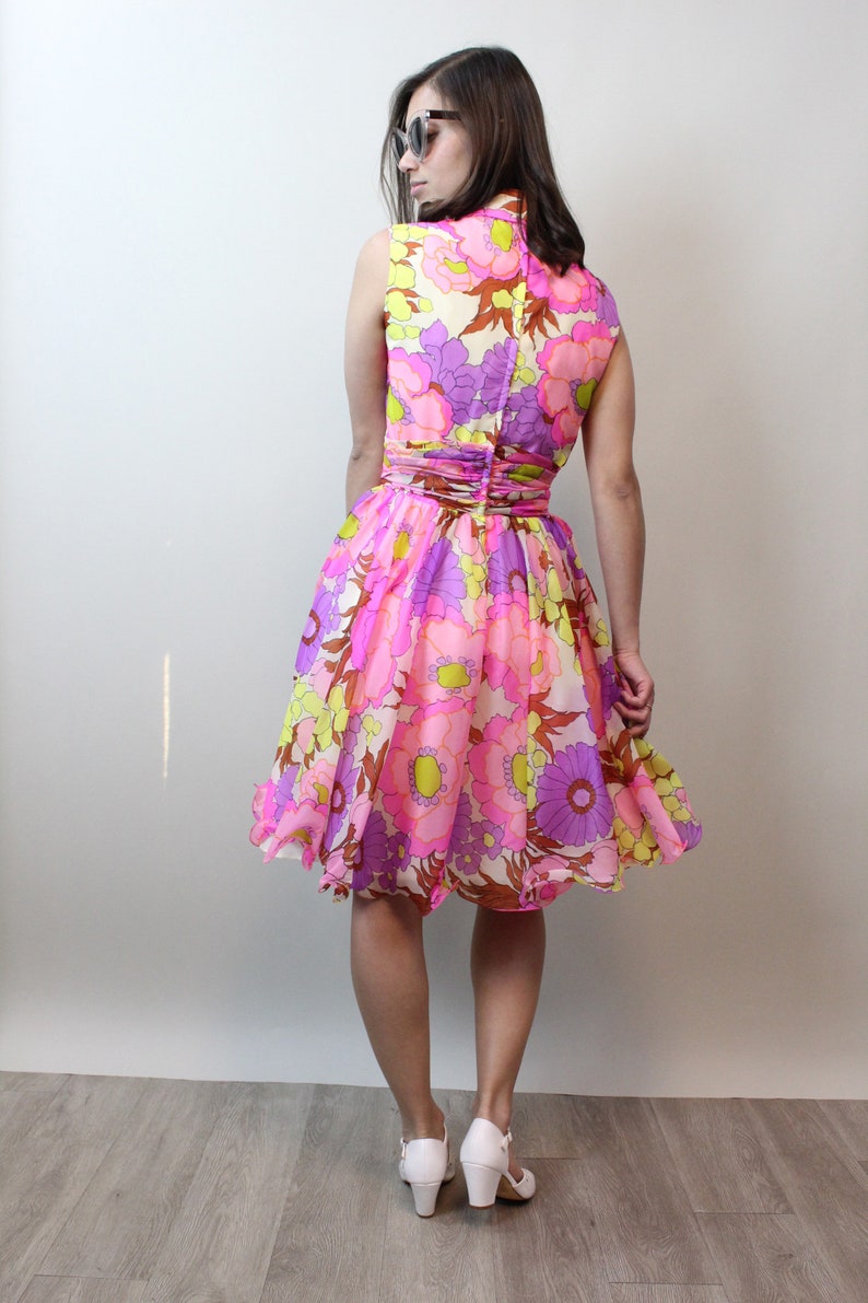 May include: A pink, purple, and yellow floral print dress with a fitted bodice and a flared skirt. The dress has a sleeveless design and a high neckline.