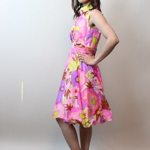 May include: A woman wearing a pink, yellow, and purple floral print dress with a white collar and a white pair of shoes.