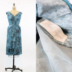 May include: A blue and white patterned sleeveless dress with a fitted bodice and a full skirt. The dress has a label that reads "Adele Simpson".