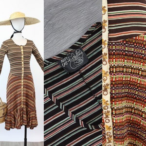 Può includere: Abito vintage a maniche lunghe con motivo a righe marrone, nero e beige. L'abito presenta un'abbottonatura frontale e una gonna svasata. L'abito è esposto su un manichino con un cappello di paglia e una borsa di vimini. Alley Cat.